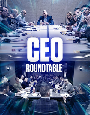 Grant Cardone CEO Roundtable with a full executive team seated at a conference table, listening attentively to a speaker. The photo shows the group from behind Grant, with one participant holding a microphone, highlighting the interactive and high-level business mastermind environment.