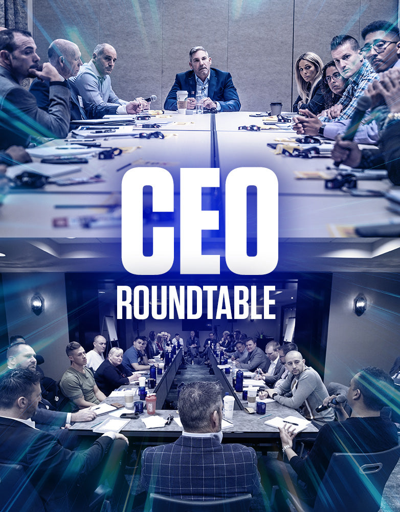 Grant Cardone CEO Roundtable with a full executive team seated at a conference table, listening attentively to a speaker. The photo shows the group from behind Grant, with one participant holding a microphone, highlighting the interactive and high-level business mastermind environment.